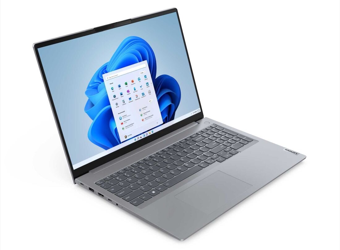 Na obrazie widoczny jest srebrny laptop z otwartym ekranem, na którym wyświetlany jest pulpit systemu Windows 11. Na obudowie znajduje się logo \'Lenovo\'.