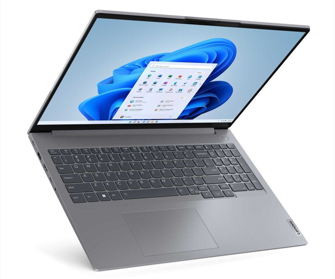 Na obrazie widoczny jest otwarty laptop z szarym korpusem i klawiaturą, na ekranie wyświetlony jest pulpit systemu Windows 11. W prawym dolnym rogu obudowy znajduje się logo \'Lenovo\'.