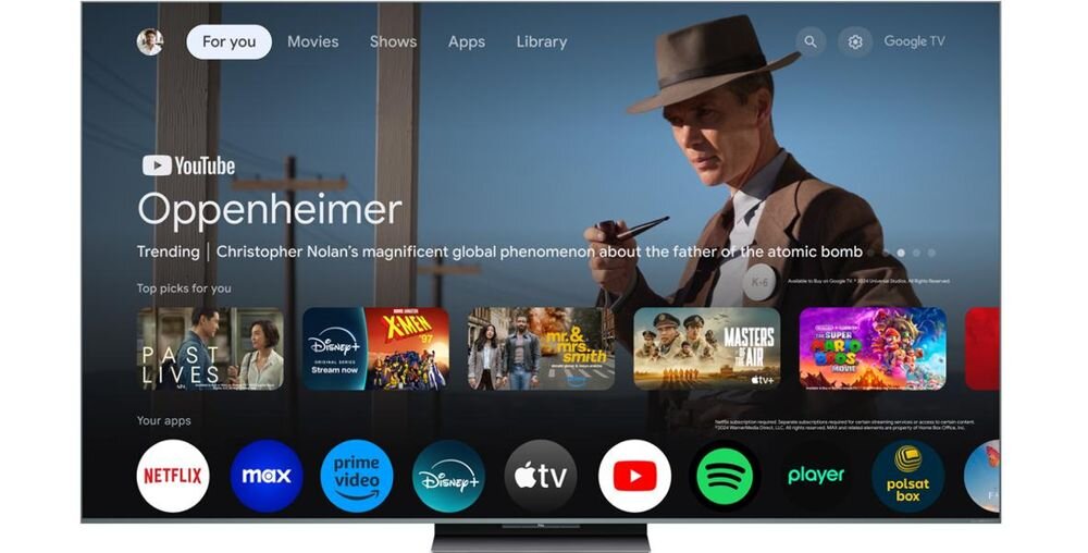 Ekran telewizora wyświetla interfejs Google TV z aplikacjami takimi jak Netflix, Prime Video, Disney+, Apple TV, YouTube, Spotify i inne. Na ekranie widoczny jest film \'Oppenheimer\' oraz lista polecanych treści.