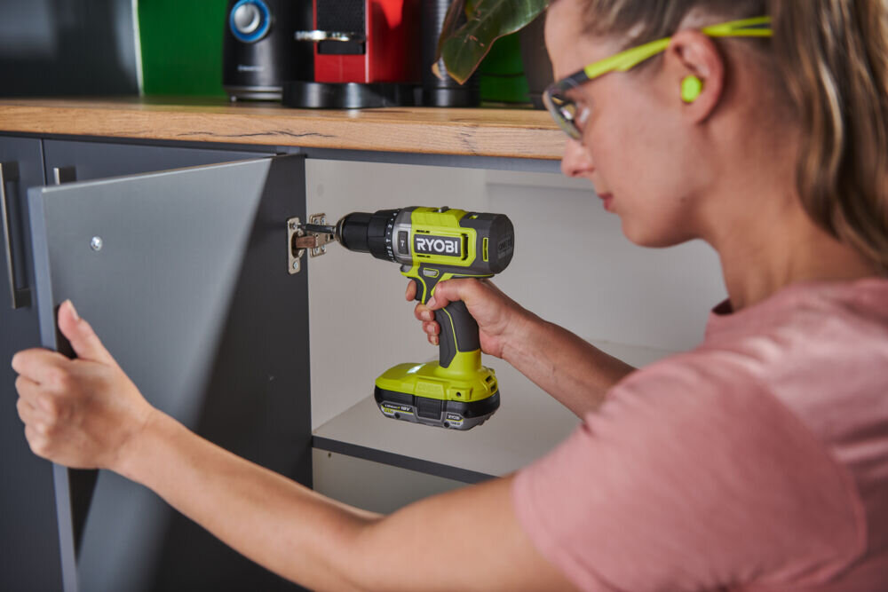 Wiertarko-wkrętarka RYOBI RPD18-2C20ST zestaw akumulatorów + Latarka z akumulatorem + Torba, narzędzia, remont, zestaw, majsterkowanie, Kobieta przykręca zawias w szafce wiertarką.