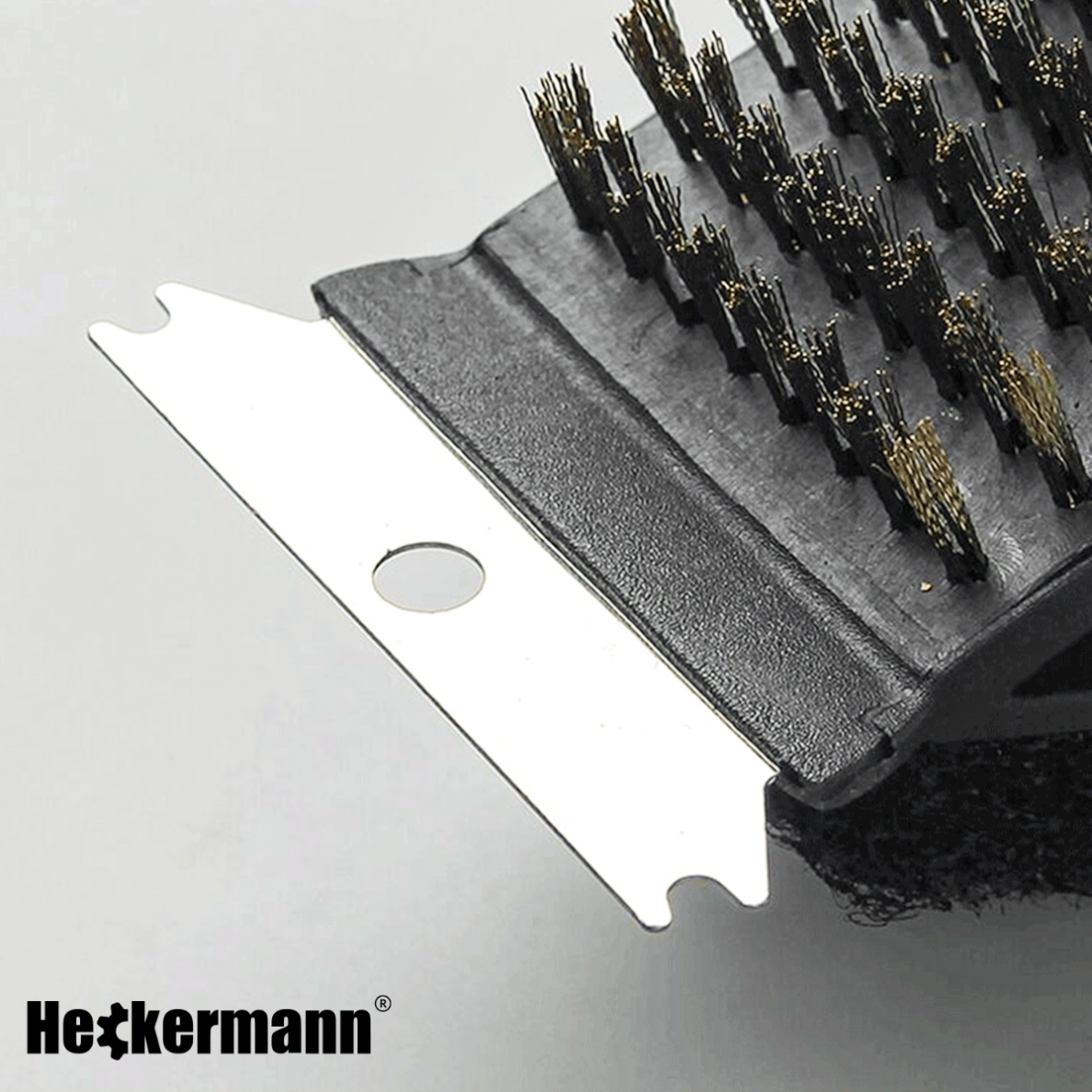 Zbliżenie na szczotkę do czyszczenia grilla z metalowym skrobakiem i włosiem. W lewym dolnym rogu widoczne jest logo \'Heckermann\'.