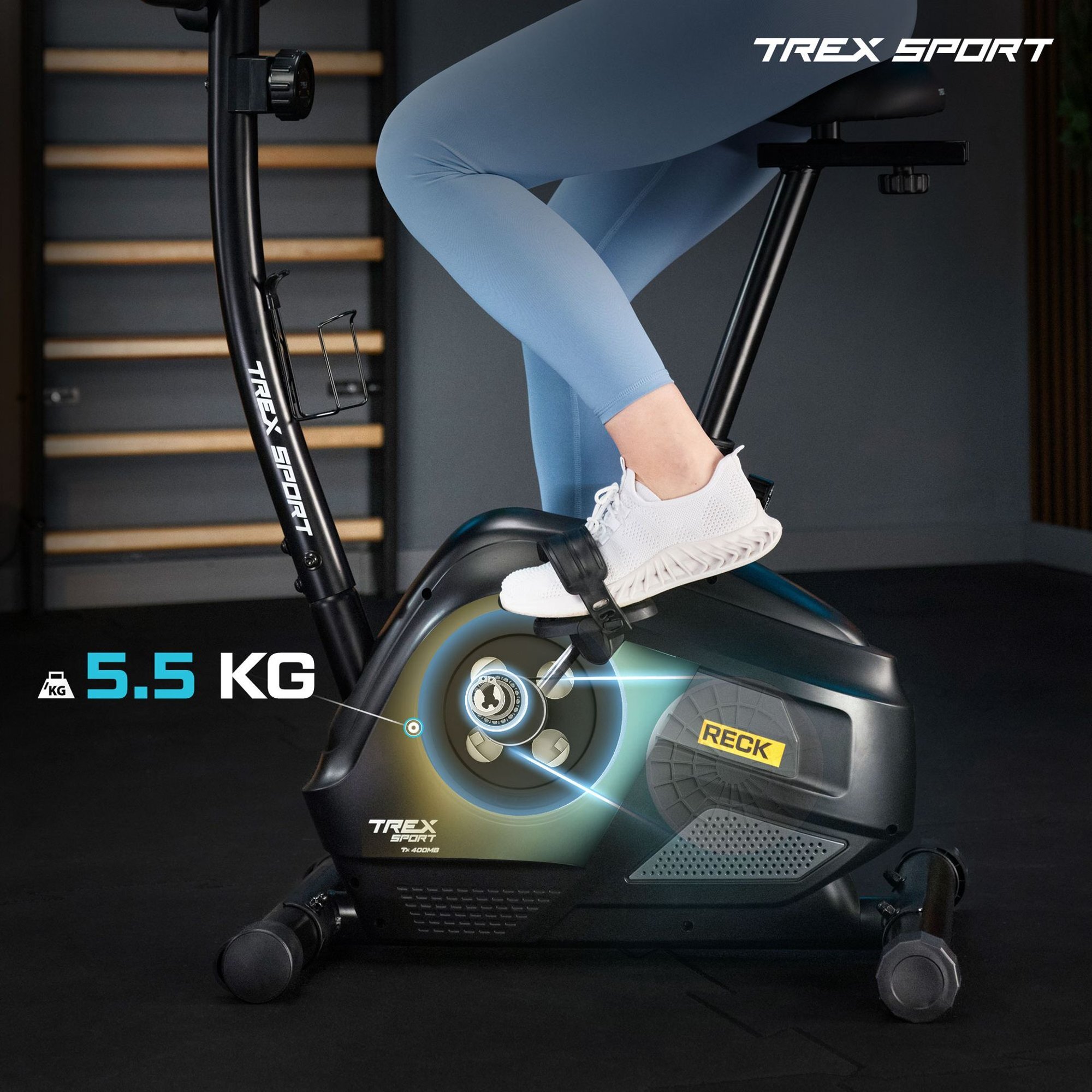 Osoba ćwiczy na rowerze stacjonarnym magnetycznym w kolorze szarym z widocznym napisem \'RECK\'. Na obrazie znajduje się również tekst \'TREX SPORT\' oraz \'5.5 KG\'.