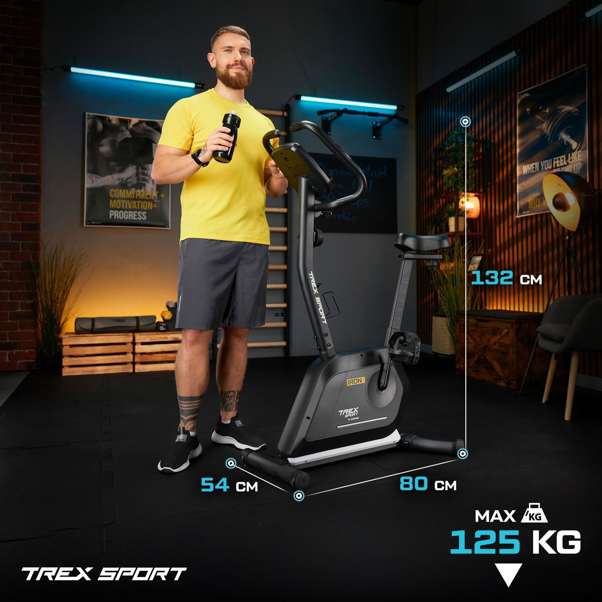 Mężczyzna w żółtej koszulce stoi obok czarnego roweru stacjonarnego IRON TX-500MB, trzymając bidon. Na obrazie widoczne są wymiary roweru: 54 cm szerokości, 80 cm długości, 132 cm wysokości oraz maksymalne obciążenie 125 kg.
