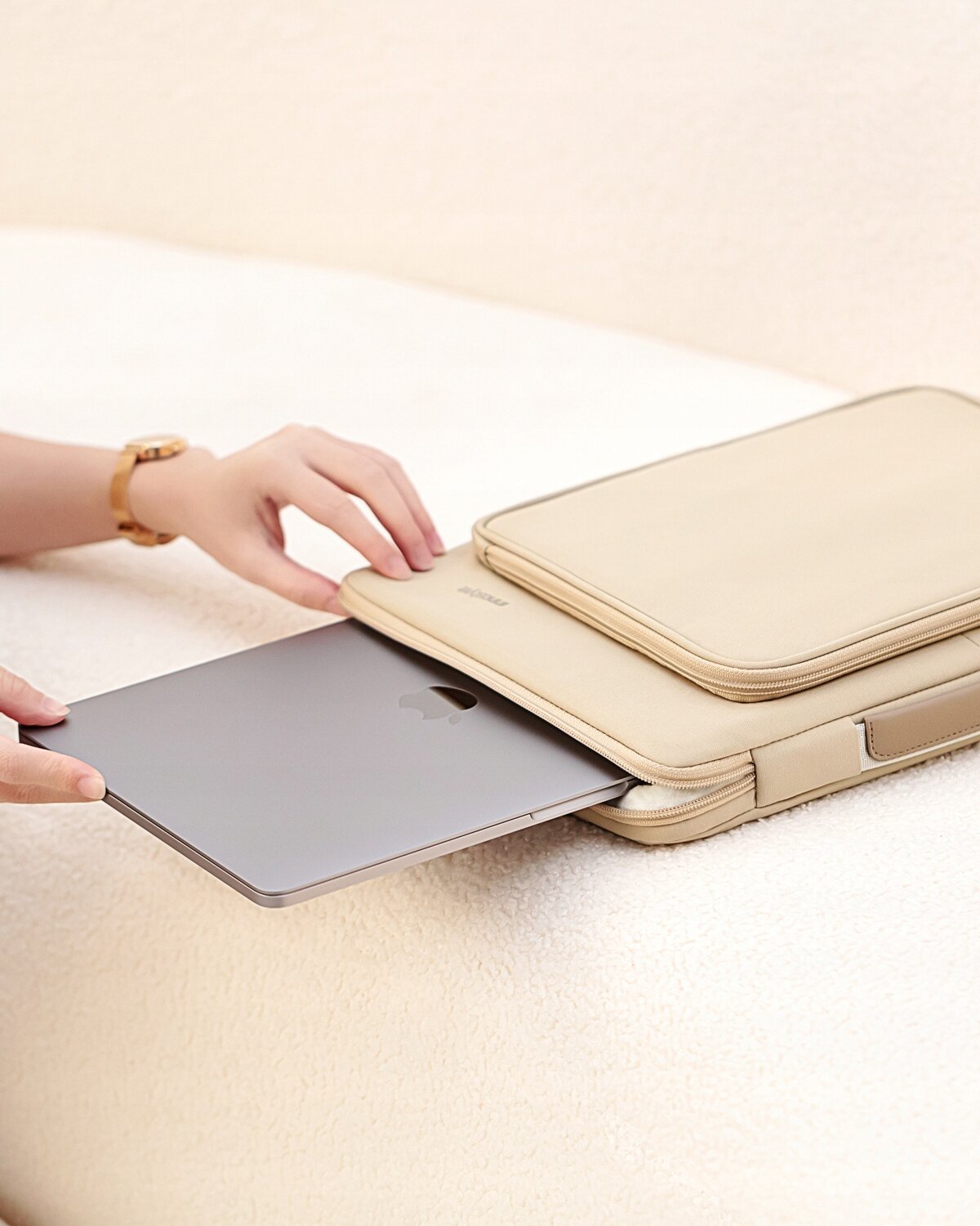 Beżowa torba na laptopa z napisem \'Innostyle\' na klapie, do której wkładany jest srebrny laptop. Tło jest jednolite i jasne, przypominające neutralne tło fotograficzne.
