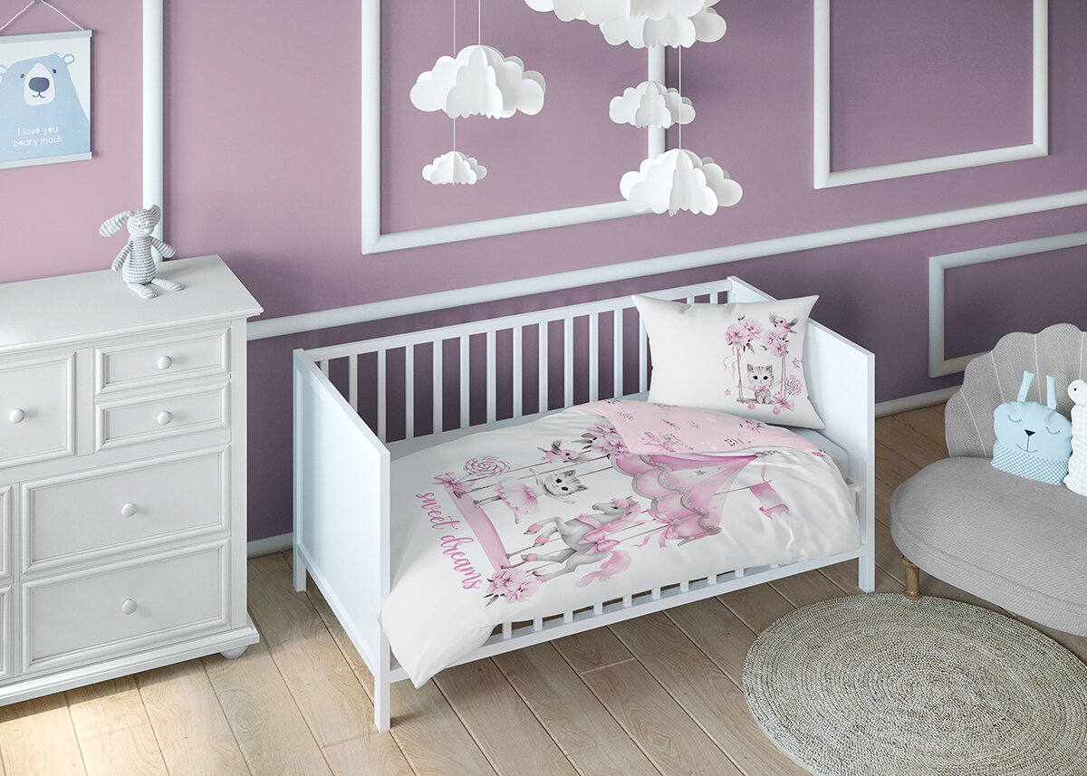 Pokój dziecięcy z białym łóżeczkiem, na którym znajduje się pościel z różowym wzorem i napisem \'sweet dreams\'. W tle fioletowa ściana z białymi ramkami i wiszącymi chmurkami, obok biała komoda i szara kanapa z poduszkami.