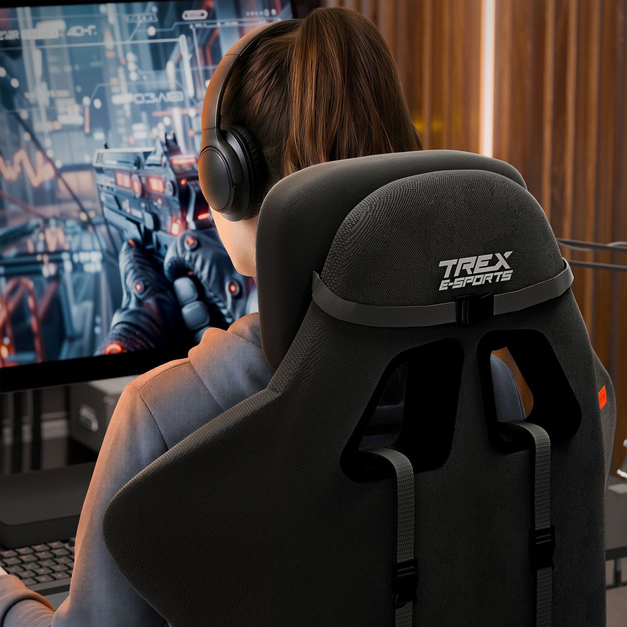 Osoba siedzi na czarnym fotelu gamingowym z napisem \'TREX E-SPORTS\', grając w grę komputerową na monitorze. Fotel ma ergonomiczny kształt i widoczne są pasy mocujące.