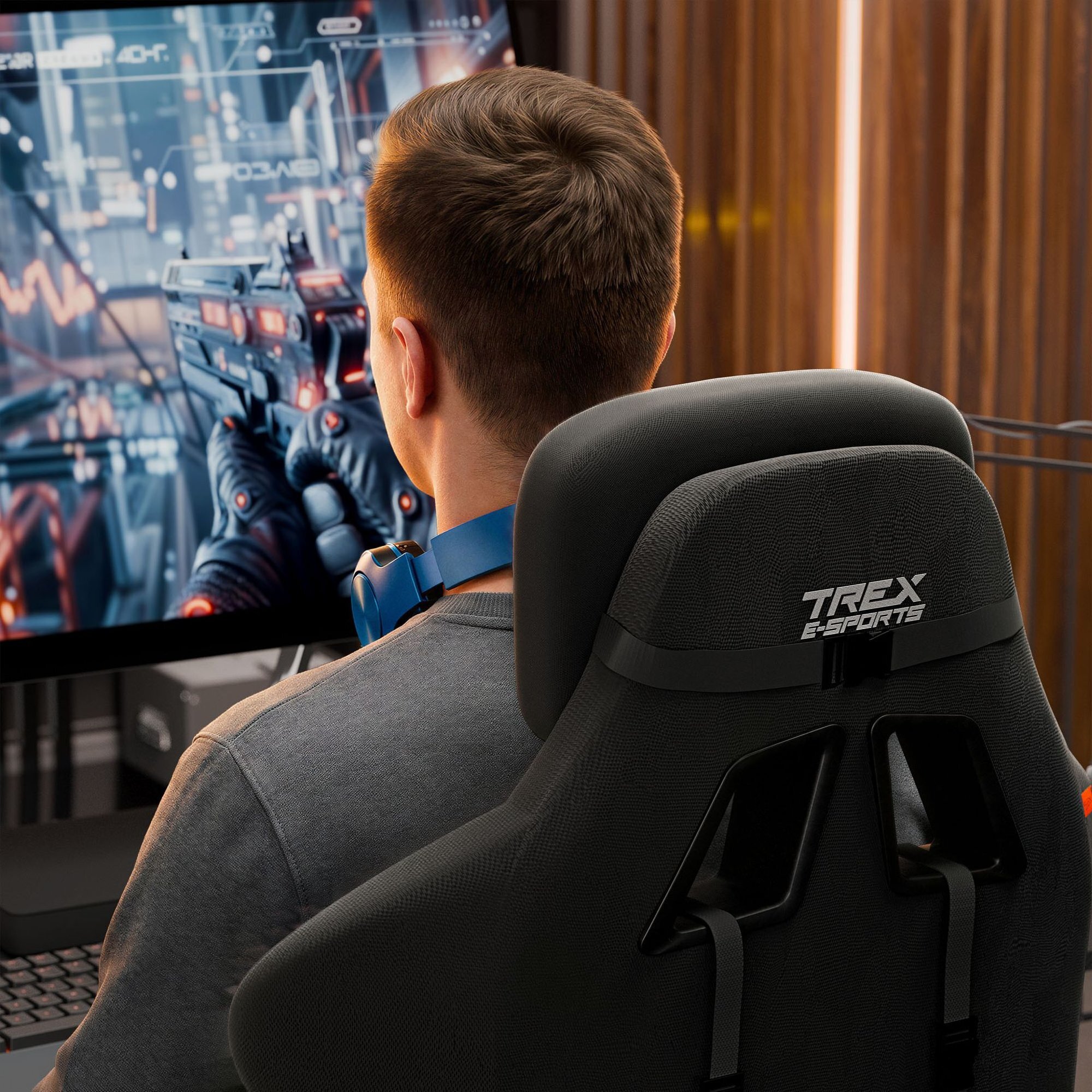 Osoba siedzi na czarnym fotelu gamingowym z napisem \'TREX E-SPORTS\', patrząc na ekran z grą wideo. Na ekranie widoczna jest postać trzymająca broń w futurystycznym otoczeniu.