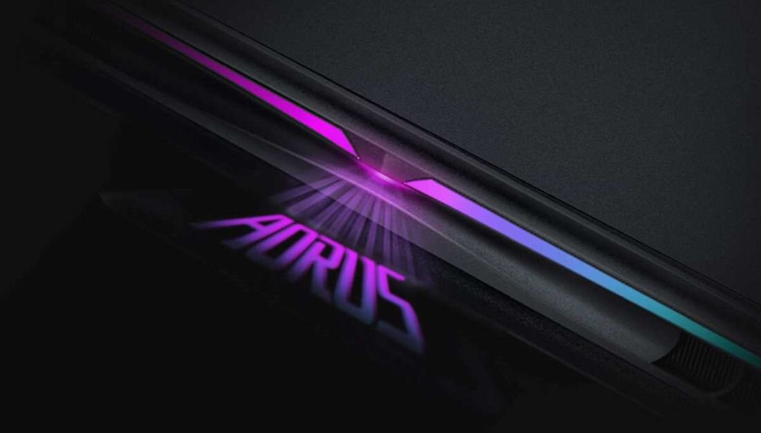 Obraz przedstawia fragment laptopa z podświetleniem w kolorach fioletowym i niebieskim. Na powierzchni widoczny jest napis \'AORUS\'.