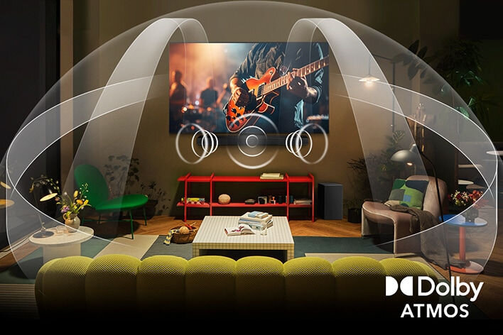 W salonie znajduje się telewizor wyświetlający obraz muzyka grającego na gitarze. W prawym dolnym rogu widoczne jest logo \'Dolby Atmos\'.