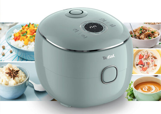 Na obrazie widoczny jest multicooker w kolorze szarym z logo \'Tefal\' na przodzie. W tle znajdują się zdjęcia różnych potraw, takich jak ryż, zupa i dania mięsne.