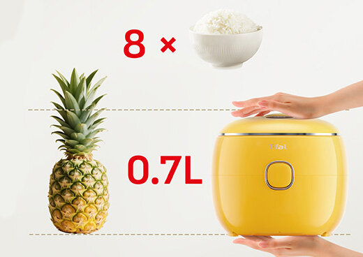 Obraz przedstawia żółty multicooker z logo Tefal, obok którego znajduje się ananas i miska z ryżem. Widoczny jest tekst: \'8 x\' oraz \'0.7L\'.