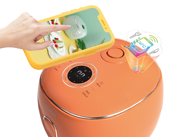 Pomarańczowy multicooker z wyświetlaczem cyfrowym i przyciskami funkcyjnymi, obok którego znajduje się ręka trzymająca żółty smartfon z wyświetlonym zdjęciem potrawy. Na urządzeniu widoczne jest logo \'Tefal\' oraz symbol NFC.
