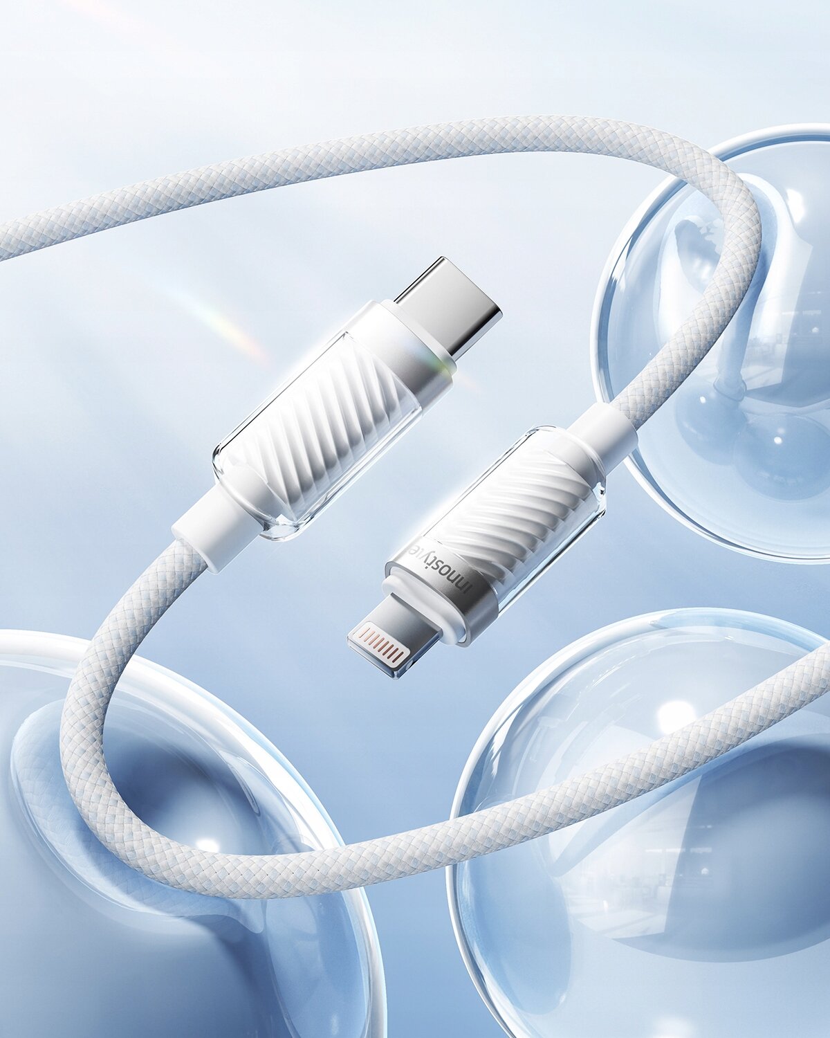 Obraz przedstawia biały kabel z końcówkami USB-C i Lightning, z plecioną osłoną, na tle niebieskich baniek. Na jednej z końcówek widoczny jest napis \'Innostyle\'.