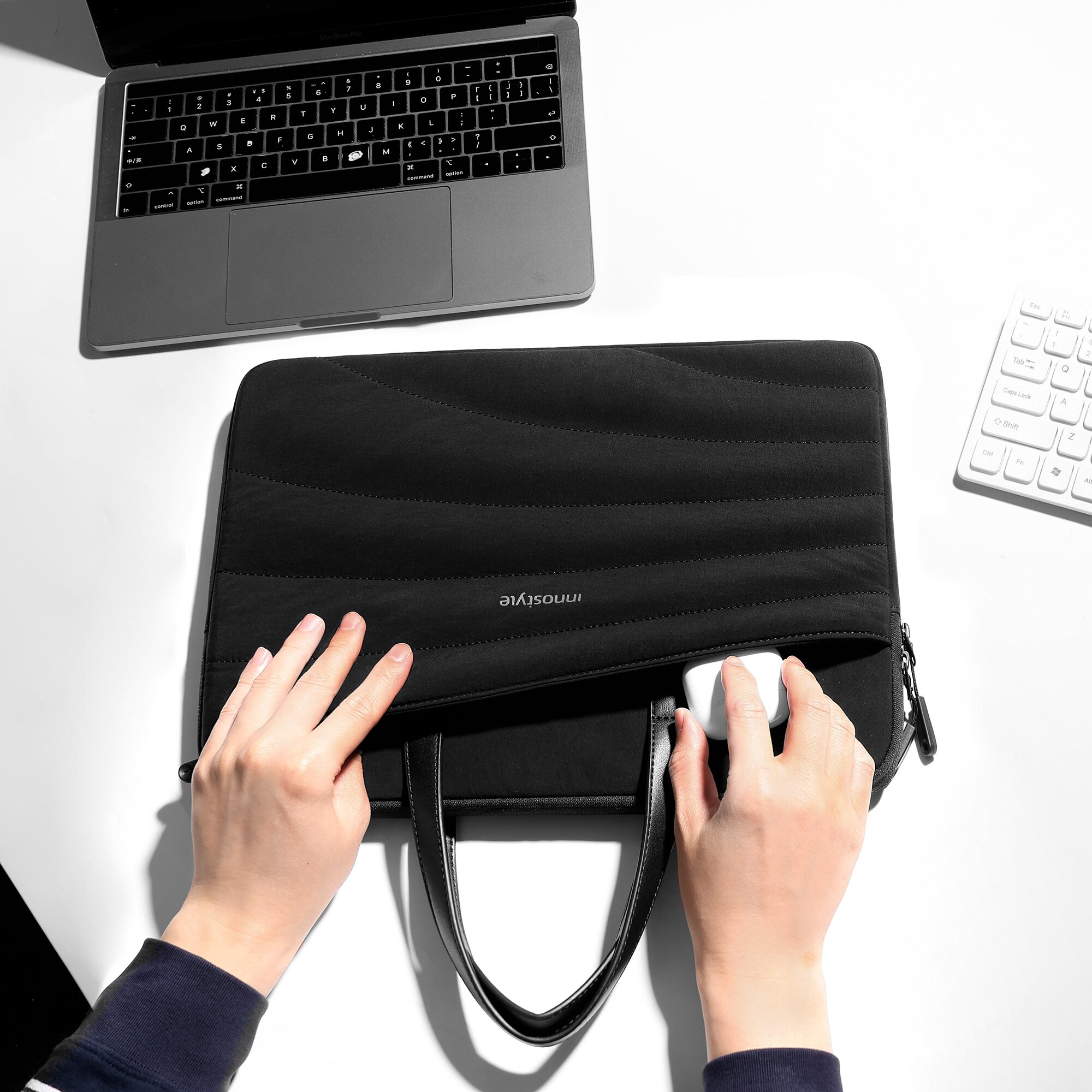 Osoba wkłada mysz komputerową do czarnej torby na laptopa z napisem \'innostyle\'. W tle widoczny jest laptop i klawiatura.