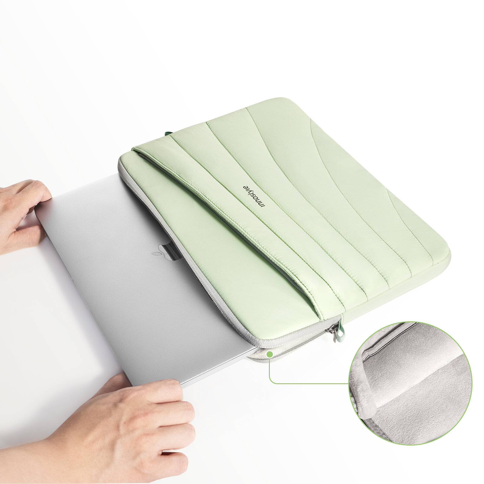 Zielona torba na laptopa z napisem \'Innostyle\' leży na białym tle, a obok niej znajduje się laptop częściowo wsunięty do torby. W prawym dolnym rogu widoczne jest powiększenie wnętrza torby, pokazujące jej miękką wyściółkę.