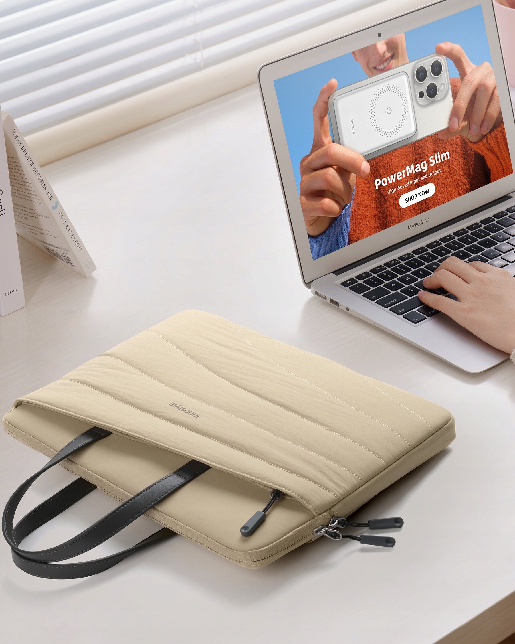 Beżowa torba na laptopa leży na biurku obok otwartego laptopa, na ekranie którego widoczny jest napis \'PowerMag Slim\' oraz przycisk \'Shop Now\'. Na torbie widoczny jest napis \'Innostyle\'.
