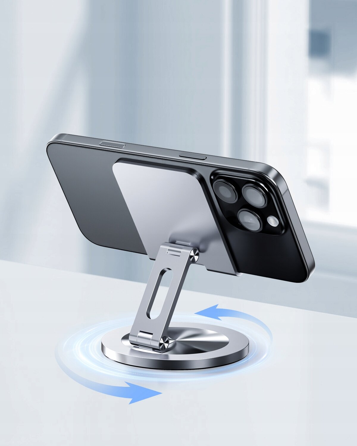 Na obrazie widoczny jest składany stojak na telefon, który podtrzymuje smartfon w pozycji poziomej. Stojak ma metaliczną podstawę z możliwością obrotu o 360 stopni, co jest zaznaczone strzałkami.