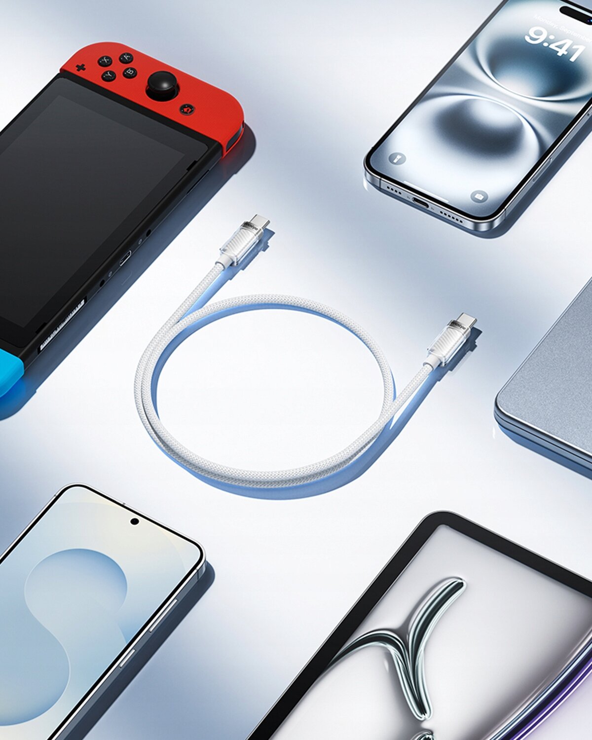 Na obrazie widoczny jest biały kabel USB-C ułożony w kształt litery U, otoczony różnymi urządzeniami elektronicznymi, takimi jak smartfony i konsola do gier. Tło jest jasne i odbija światło.