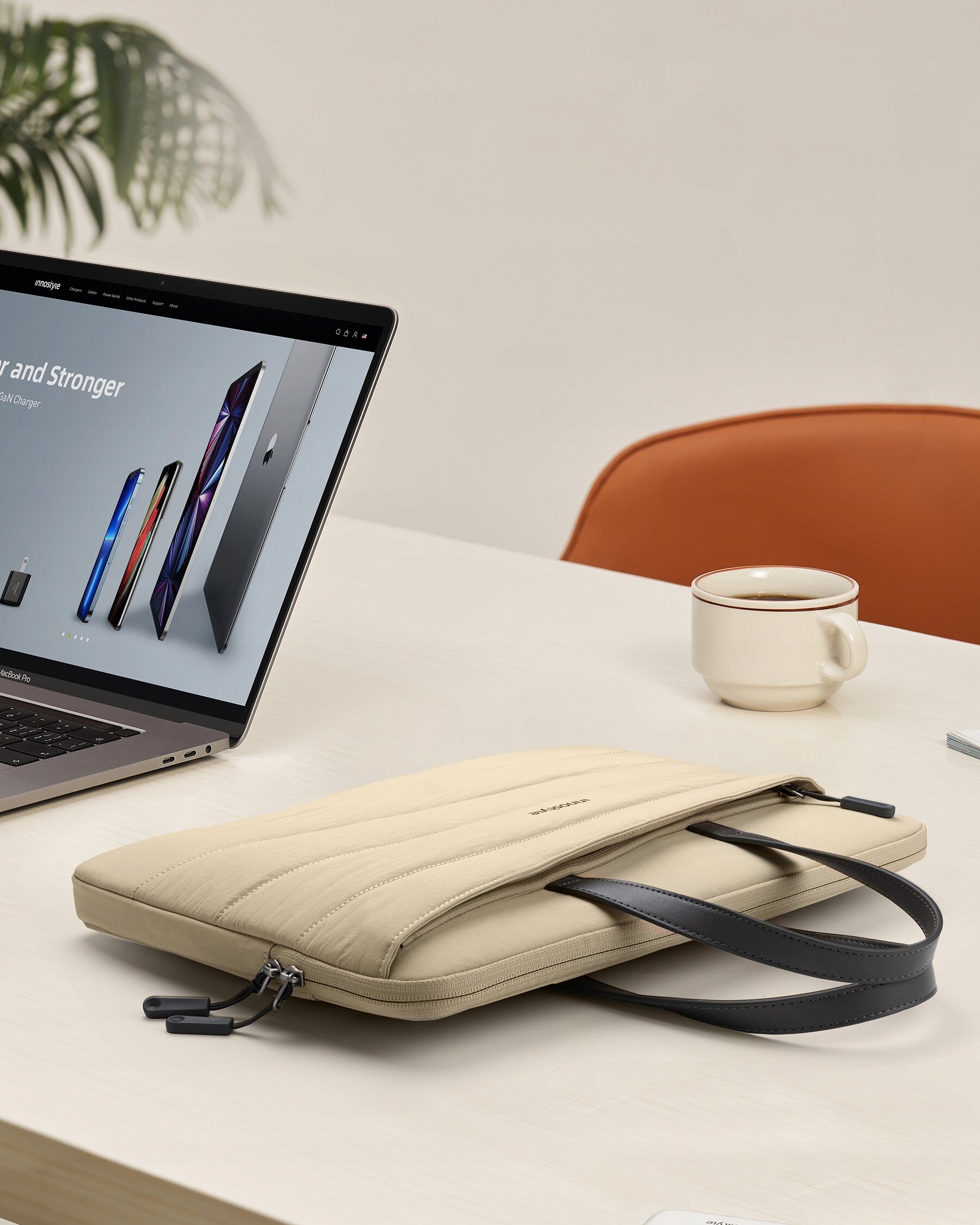 Beżowa torba na laptopa leży na biurku obok otwartego laptopa z widoczną stroną internetową oraz filiżanki z kawą. Na torbie widoczny jest napis \'Innostyle\'.