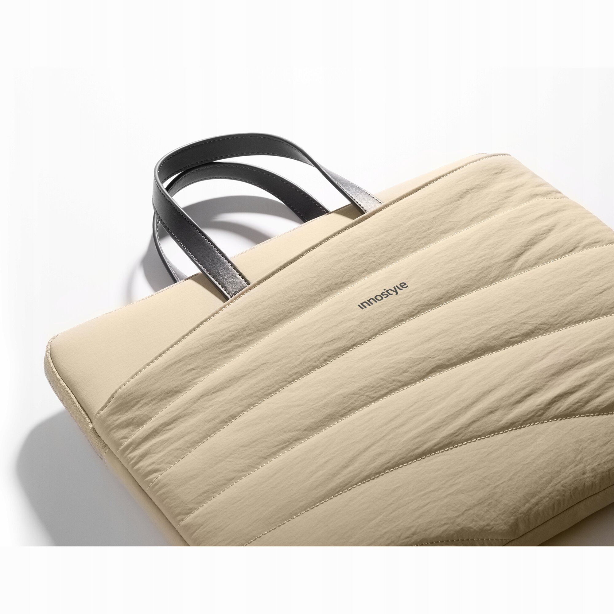 Beżowa torba na laptopa z czarnymi uchwytami, z widocznym logo \'innostyle\' na powierzchni.