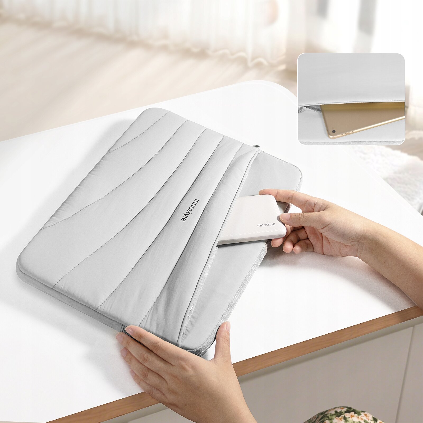 Szara torba na laptopa z napisem \'innostyle\' leży na białym stole, a osoba wkłada do niej urządzenie. W prawym górnym rogu znajduje się zbliżenie na kieszeń torby z widocznym urządzeniem w środku.