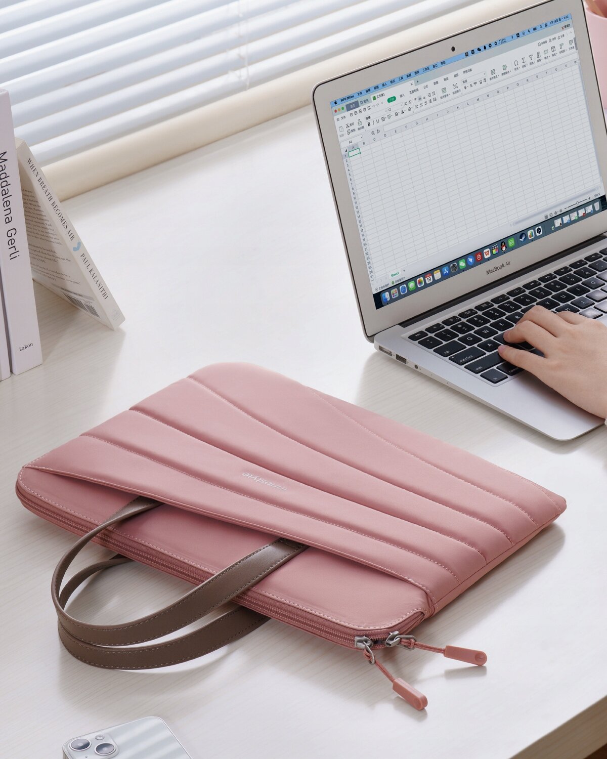 Różowa torba na laptopa leży na biurku obok otwartego laptopa, na którym widoczny jest arkusz kalkulacyjny. Na torbie znajduje się napis \'Carrylite\'.