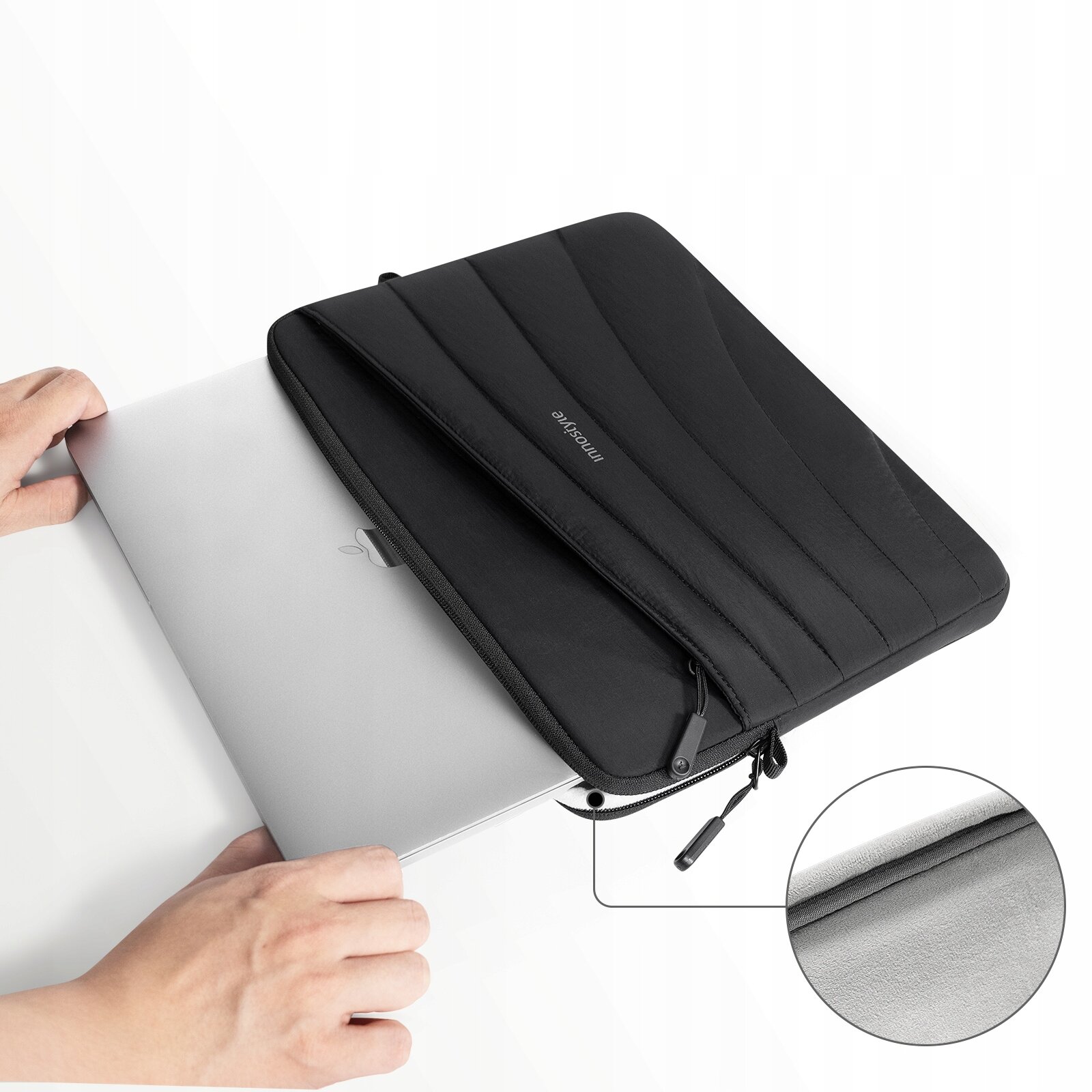 Czarna torba na laptopa z napisem \'innostyle\' jest otwarta, a w jej wnętrzu znajduje się srebrny laptop. W prawym dolnym rogu znajduje się powiększenie materiału torby.