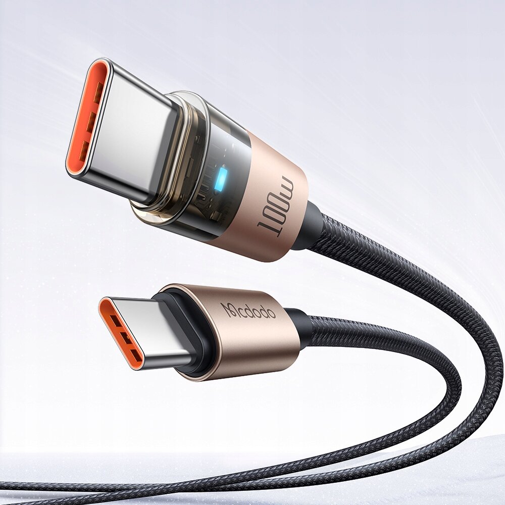 Zdjęcie przedstawia złoty kabel USB-C z napisem \'100W\' na jednym z końców oraz logo \'Mcdodo\' na drugim. Kabel ma plecioną osłonę i jest umieszczony na neutralnym tle.