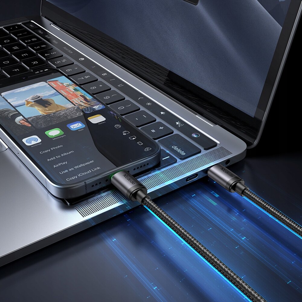 Na zdjęciu widać laptopa z podłączonym telefonem za pomocą kabla USB-C, na ekranie telefonu widoczne są opcje takie jak \'Copy Photo\', \'Add to Album\', \'AirPlay\', \'Use as Wallpaper\', \'Copy iCloud Link\'. Kabel ma widoczne logo \'Mcdodo\' na złączu.
