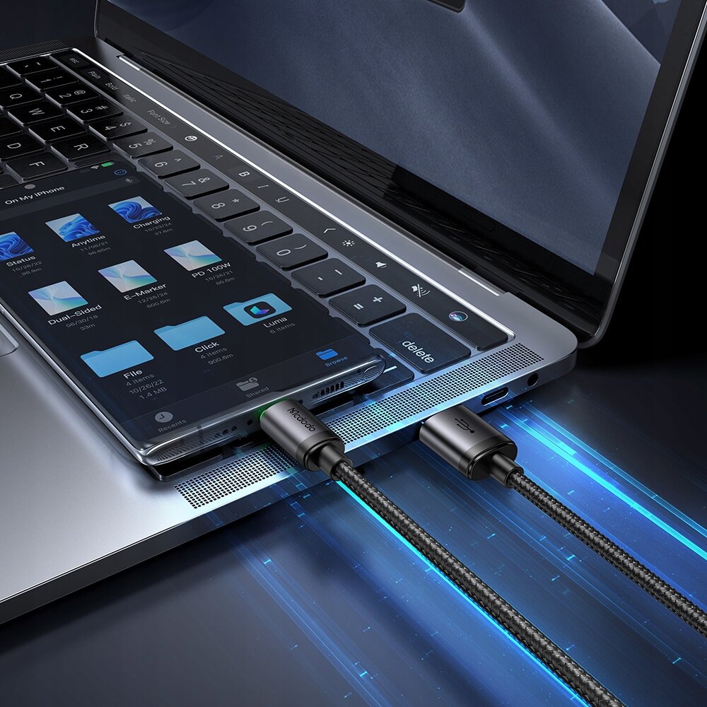 Zdjęcie przedstawia laptop z otwartym ekranem, na którym leży smartfon z widocznymi ikonami aplikacji. Do laptopa i smartfona podłączony jest kabel z napisem \'Mcdodo\'.