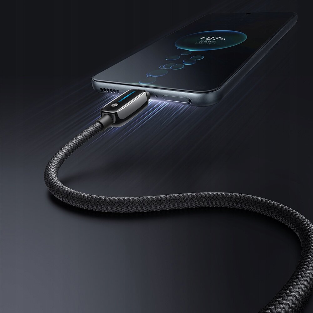 Obraz przedstawia telefon podłączony do kabla USB-C z plecionym oplotem, który emituje niebieskie światło. Na ekranie telefonu widoczny jest wskaźnik ładowania z napisem \'87%\'.
