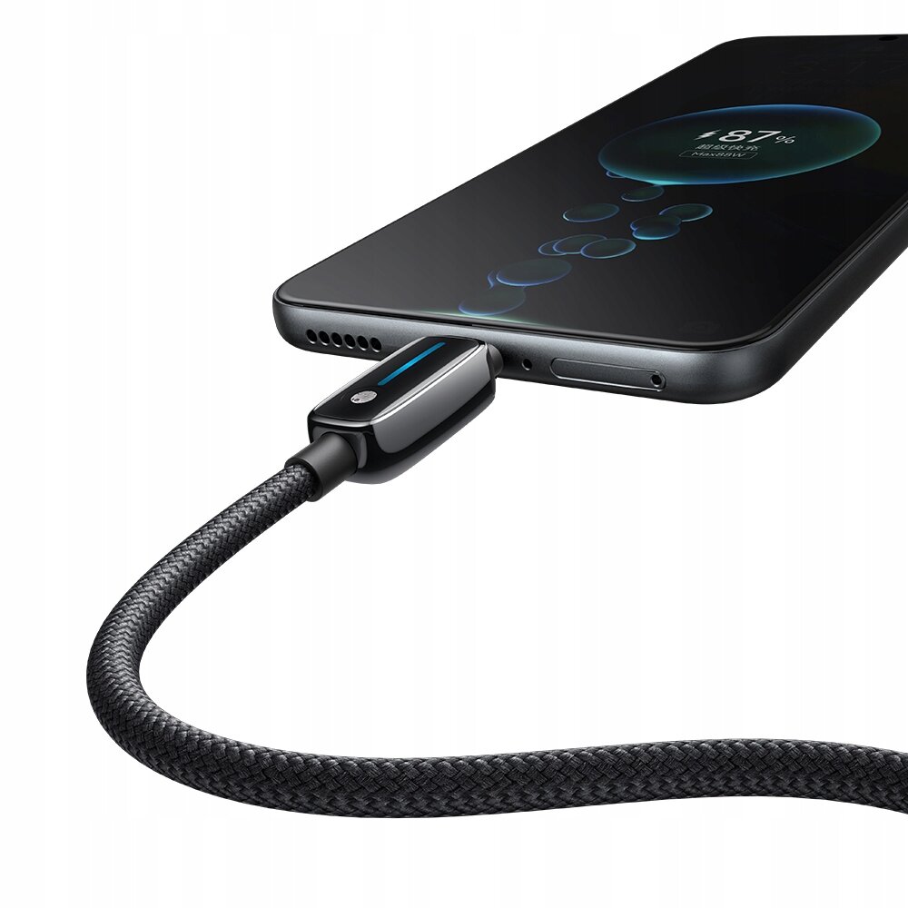 Czarny kabel USB-C podłączony do smartfona, na ekranie którego widoczny jest wskaźnik ładowania na poziomie 87%.