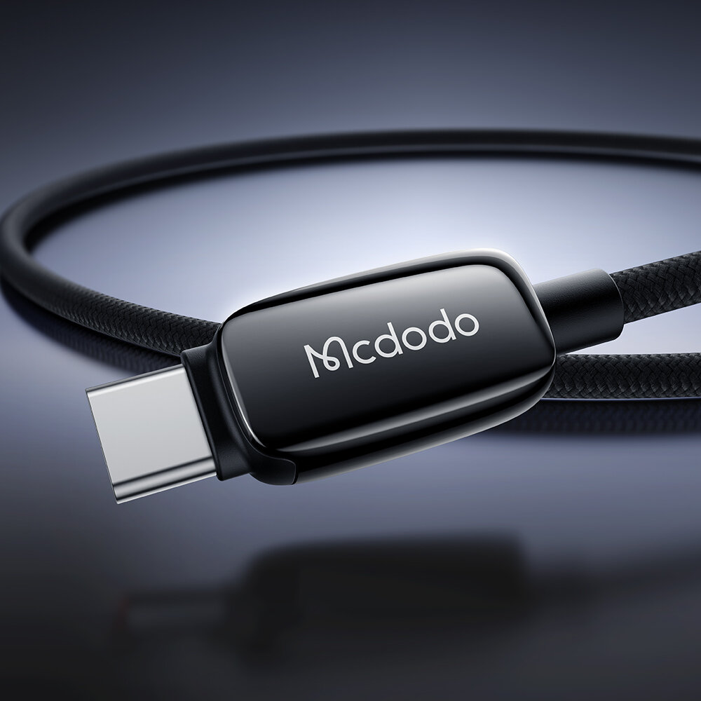 Zbliżenie na czarny kabel USB-C z logo \'Mcdodo\' na obudowie wtyczki, na tle gradientu od ciemnego do jasnego koloru.