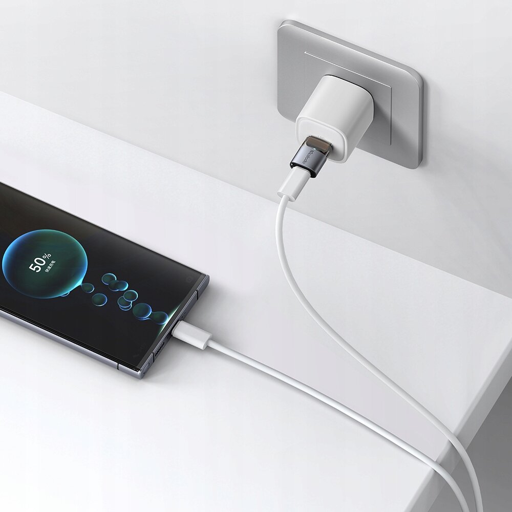 Telefon podłączony do ładowarki za pomocą białego kabla USB-C, z wyświetlaczem pokazującym 50% naładowania. Adapter USB-A do USB-C jest wpięty do gniazdka ściennego.