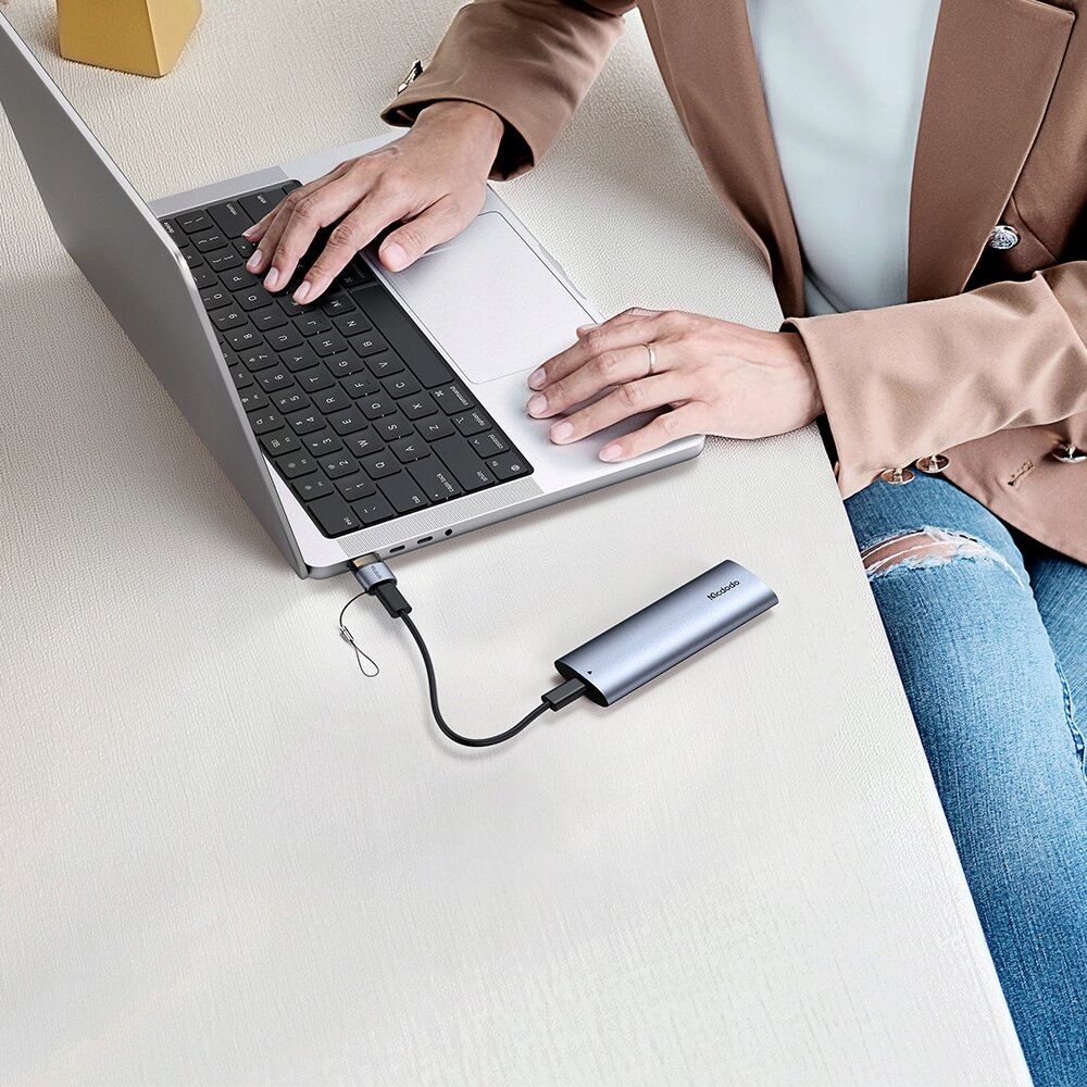 Osoba pracująca na laptopie, do którego podłączony jest adapter Mcdodo z napisem \'Mcdodo\' na obudowie.