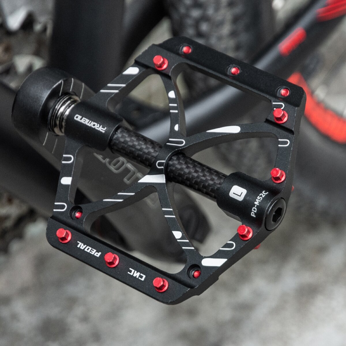 Na zdjęciu widoczne są czarne, aluminiowe pedały rowerowe platformowe z czerwonymi pinami. Na pedale znajduje się tekst: \'CNC PEDAL\'.