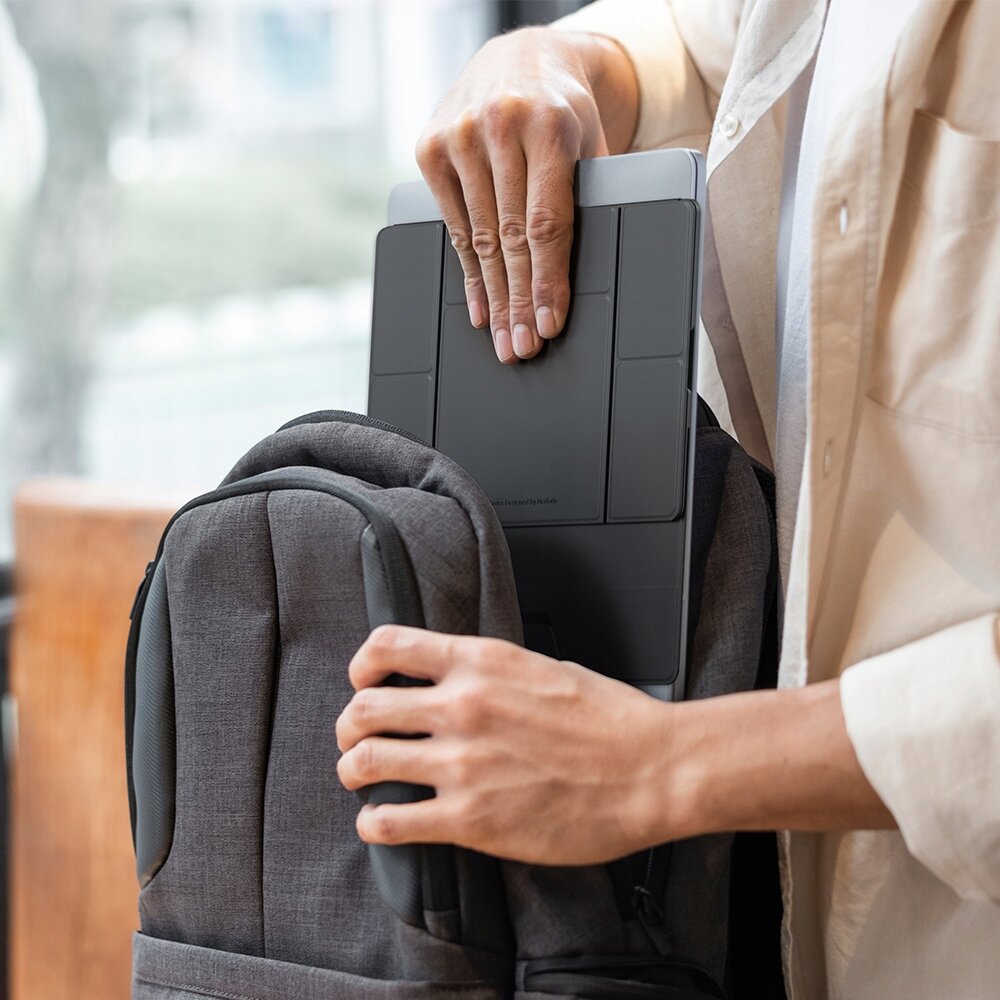 Osoba wkładająca czarną podstawkę pod laptopa do szarego plecaka.