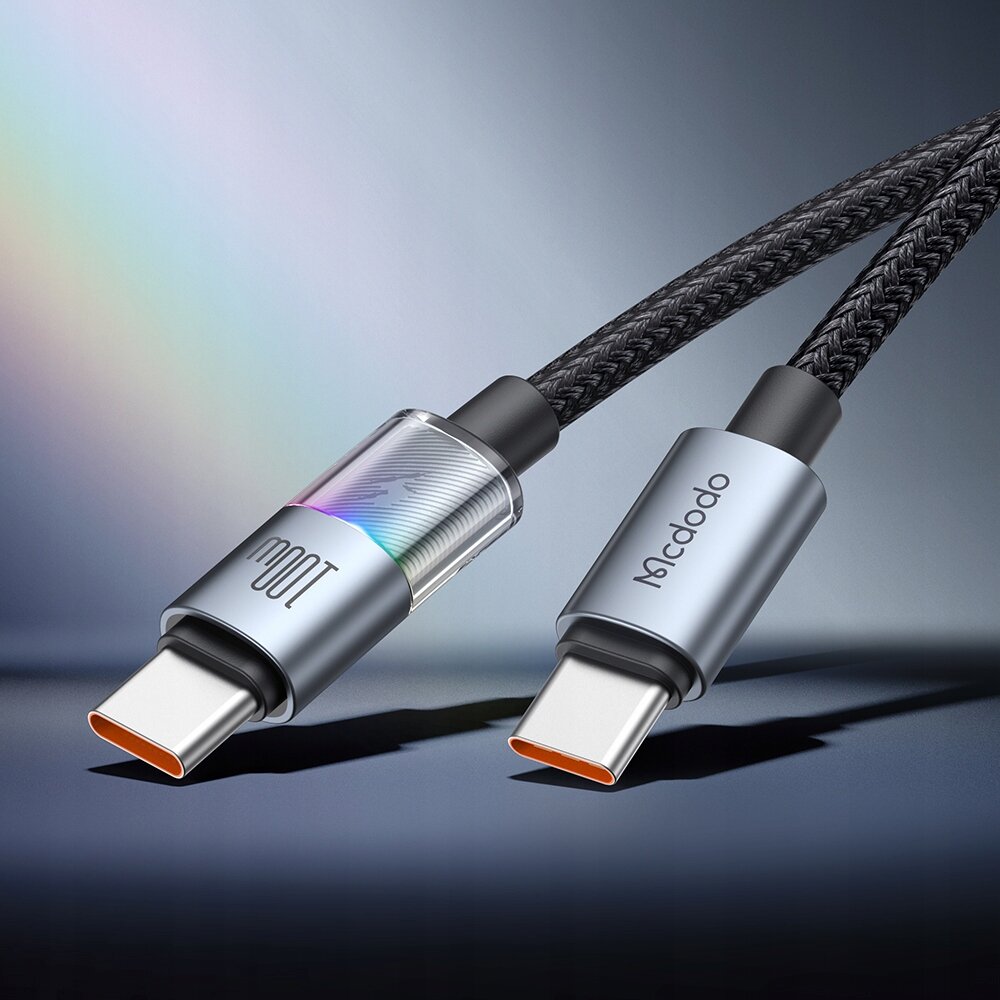 Obraz przedstawia dwa końce kabla USB-C z metalowymi wtyczkami, na jednej z nich widoczne jest logo \'Mcdodo\'. Kabel ma plecioną, czarną osłonę.
