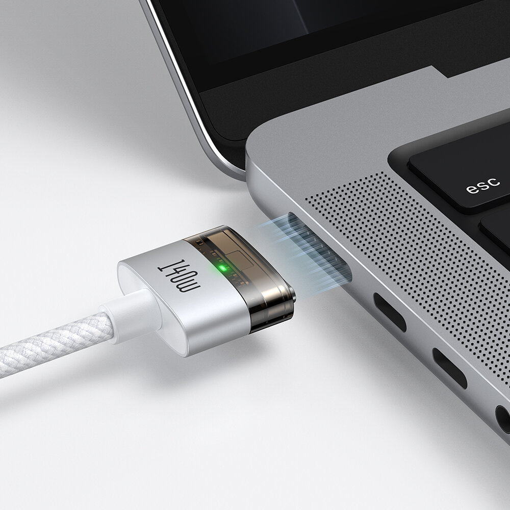 Obraz przedstawia kabel zasilający z końcówką magnetyczną z napisem \'140W\', podłączany do laptopa. Na końcówce kabla świeci się zielona dioda.