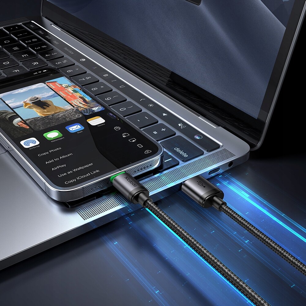 Zdjęcie przedstawia telefon podłączony do laptopa za pomocą kabla USB Lightning, na ekranie telefonu widoczne są opcje udostępniania zdjęcia. Na kablu znajduje się napis \'Mcdodo\'.
