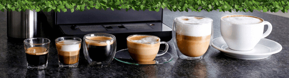 Na blacie stoi ekspres do kawy oraz sześć filiżanek z różnymi rodzajami kawy, w tym espresso i cappuccino. W tle widoczna jest dekoracja z zielonych liści.