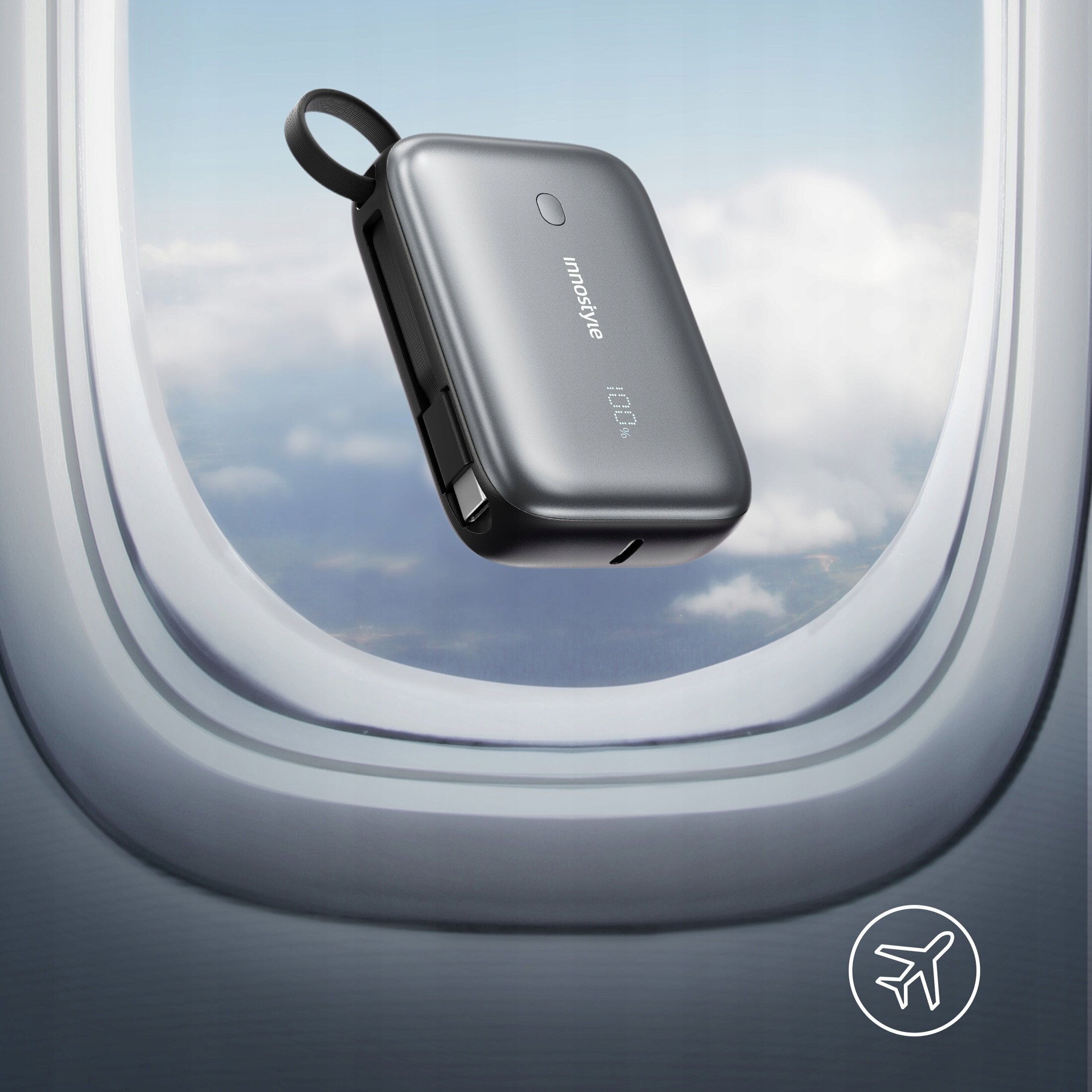 Na tle okna samolotu widać szary powerbank z napisem \'innostyle\' i wskaźnikiem \'100%\'. W prawym dolnym rogu znajduje się ikona samolotu.