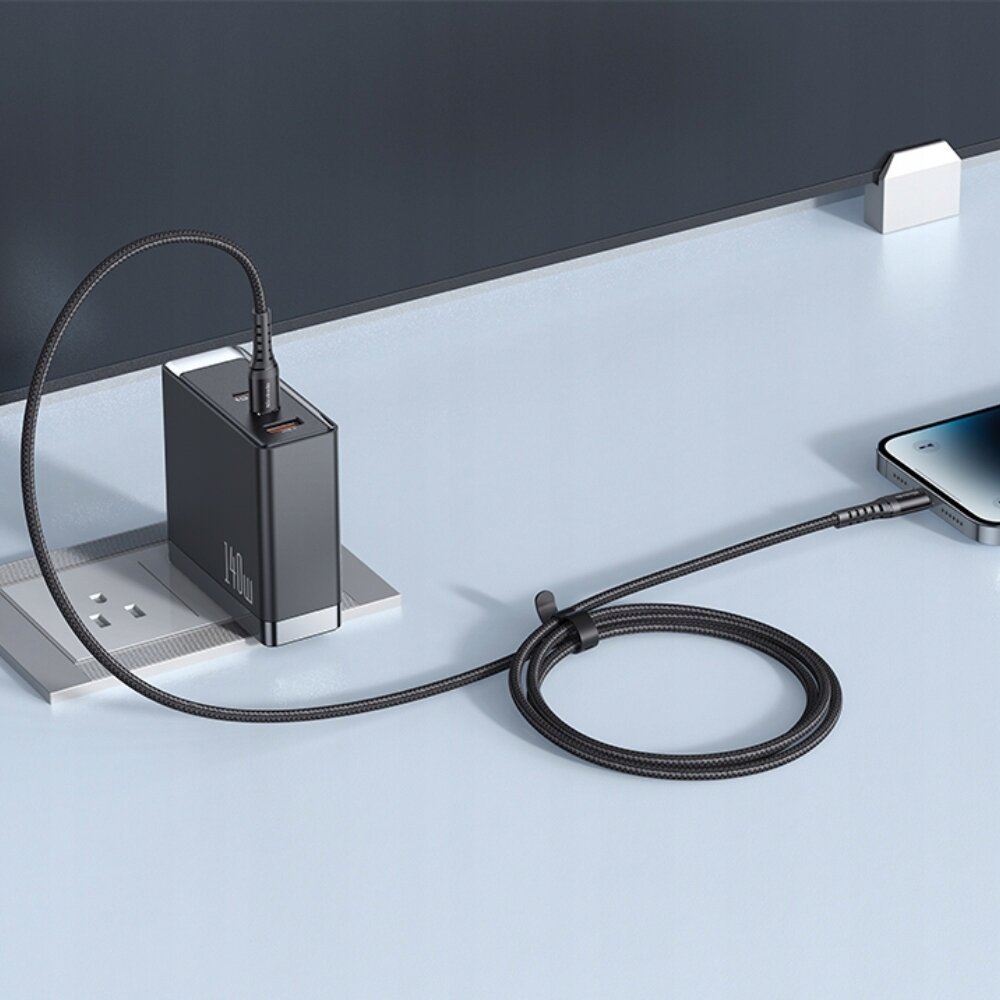 Na obrazie widać czarną ładowarkę z logo \'Mcdodo\' podłączoną do gniazdka, z której wychodzi długi kabel USB-C podłączony do smartfona. Ładowarka i kabel znajdują się na jasnej powierzchni.