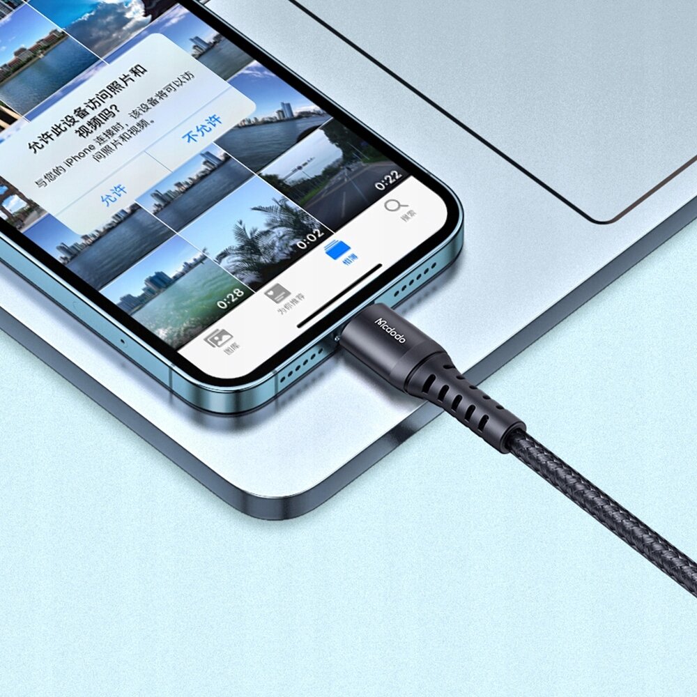 Zdjęcie przedstawia telefon podłączony do ładowarki kablem USB-C Lightning, na ekranie widoczne są miniatury zdjęć oraz tekst w języku chińskim. Na wtyczce kabla widoczny jest napis \'Mcdodo\'.