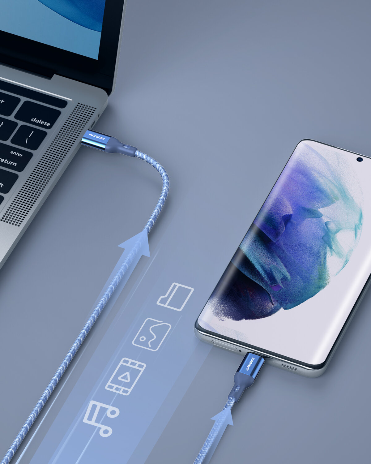 Na obrazie widać laptopa i smartfon połączone niebieskim kablem USB-C z napisem \'innostyle\'. Kabel jest podłączony do obu urządzeń, a obok widoczne są ikony symbolizujące przesył danych.