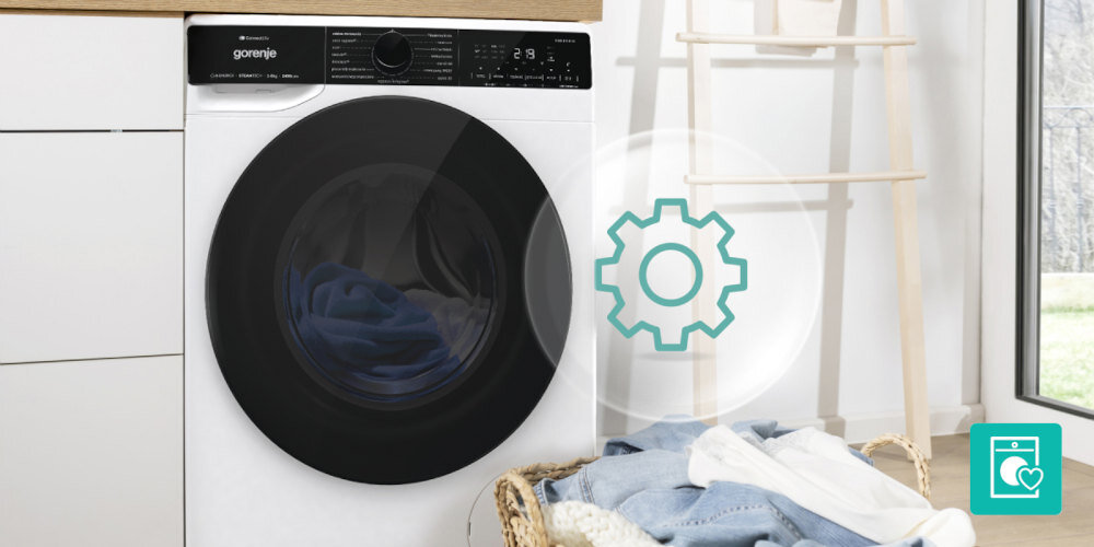 Na obrazie widoczna jest pralka z logo \'gorenje\' na panelu sterowania, obok której znajduje się kosz z praniem. Na obrazie widoczna jest również ikona z symbolem koła zębatego.