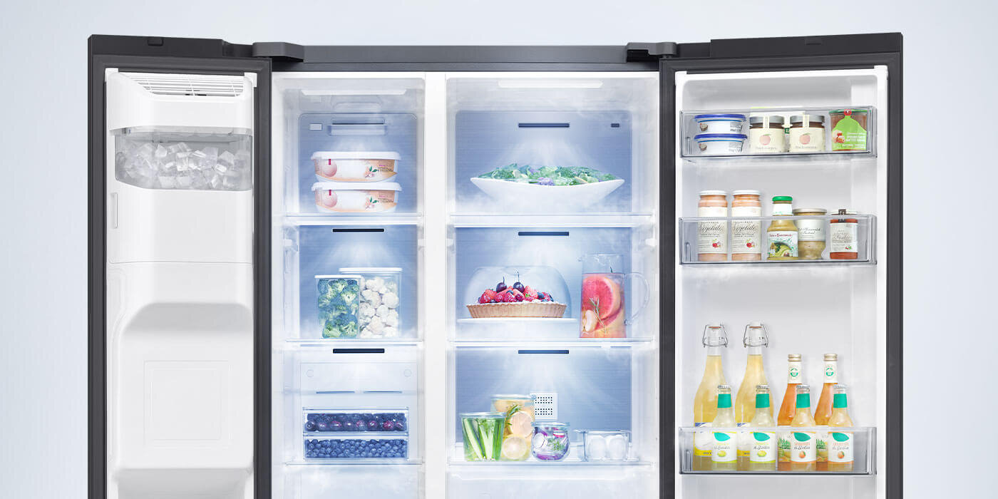 RS70F64KEBEO – lodówka Side by Side Samsung z równomiernym chłodzeniem All-Around Cooling Otwarta lodówka z widocznymi półkami wypełnionymi różnymi produktami spożywczymi, takimi jak owoce, warzywa, napoje i pojemniki z żywnością. Po lewej stronie znajduje się kostkarka do lodu.