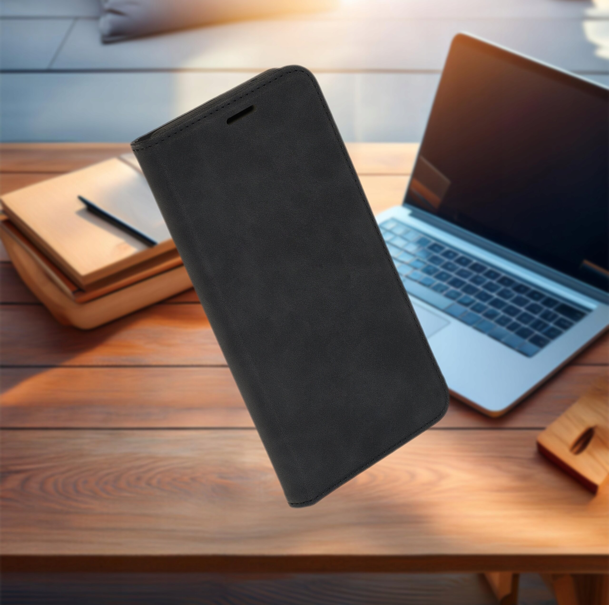 Czarne etui z klapką do telefonu, unoszące się nad drewnianym biurkiem, na którym znajduje się otwarty laptop i notes z długopisem.