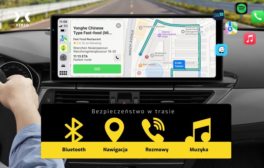 Na desce rozdzielczej samochodu zamontowany jest tablet z mapą nawigacyjną i informacjami o restauracji. Na dole ekranu widnieje napis \'Bezpieczeństwo w trasie\' oraz ikony z podpisami: Bluetooth, Nawigacja, Rozmowy, Muzyka.