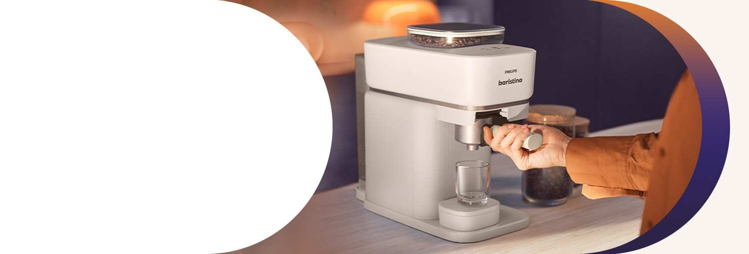 Ekspres do kawy PHILIPS Baristina BAR300/00 z widocznym logo, z zautomatyzowanym procesem mielenia i zaparzania, na blacie kuchennym. Osoba trzyma uchwyt portafiltra, a w tle widoczne są rozmyte elementy kuchni.